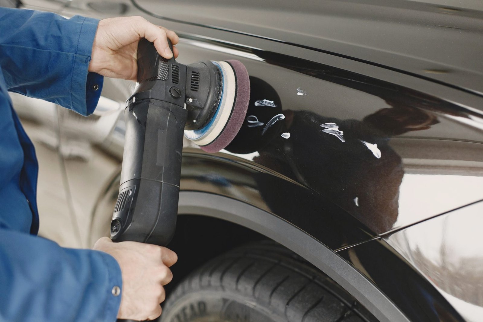 A powered buffing head worked across a painted body panel.