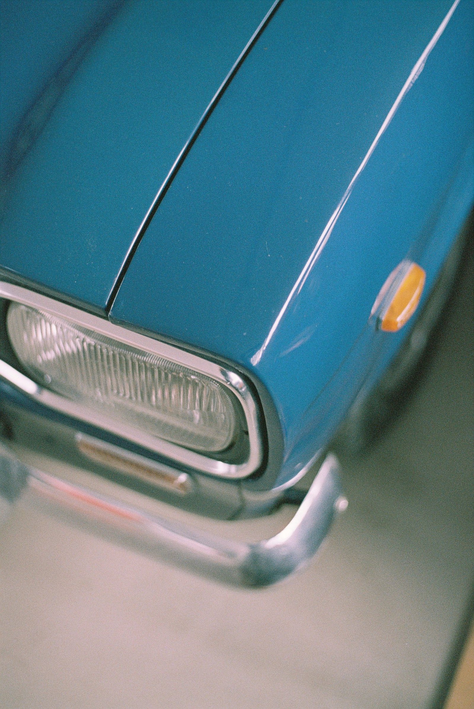 The front of a pale blue classic car with chrome trim and headlight rings.